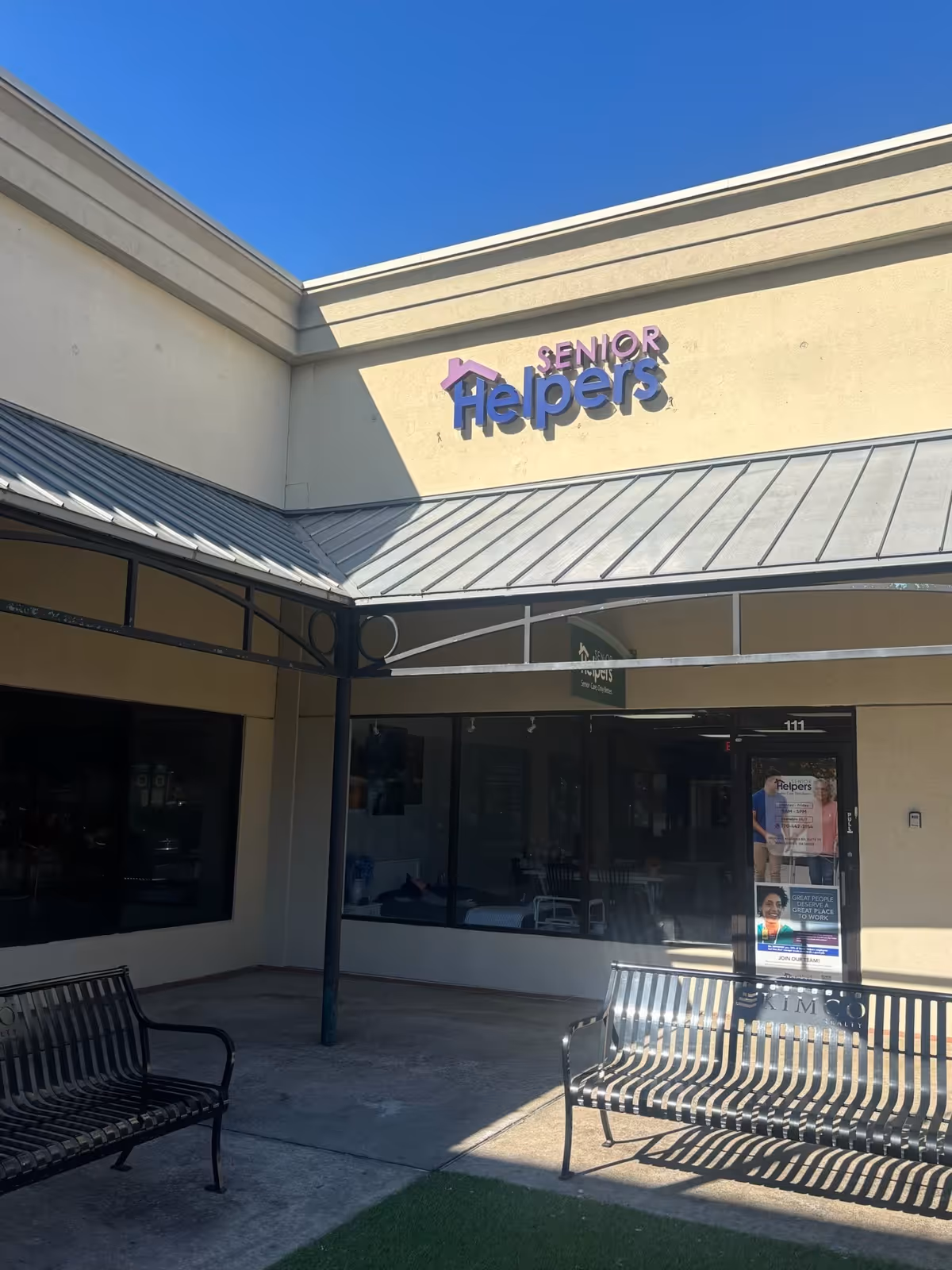 Exterior view of a Senior Helpers facility with benches and a glass storefront entrance.