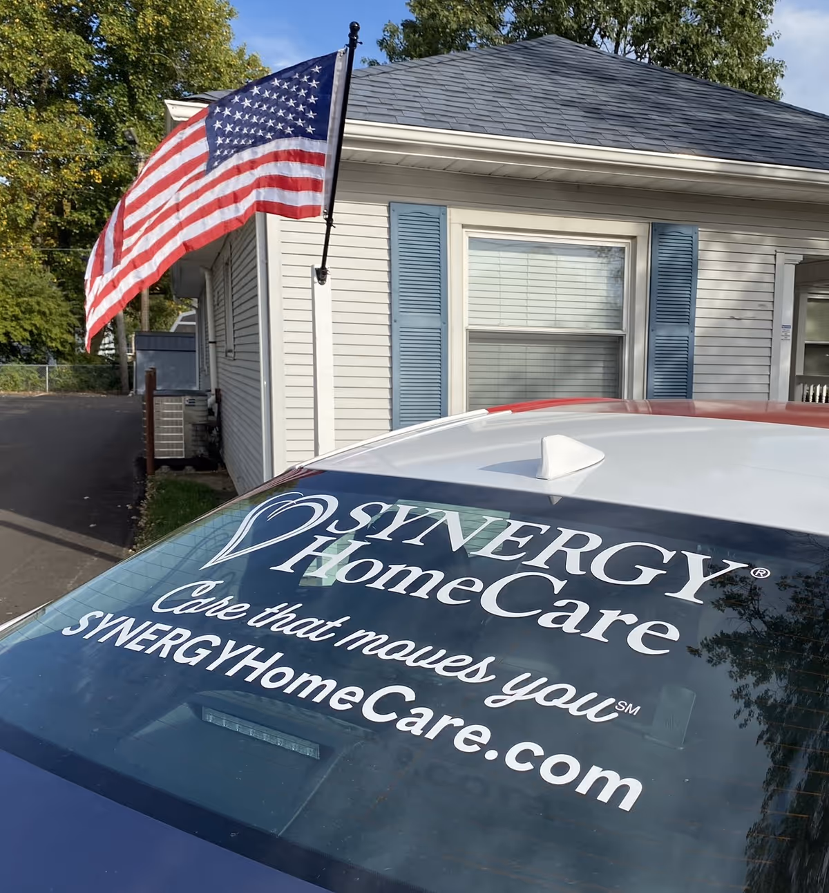 Exterior view of a Synergy HomeCare building with an American flag and branded vehicle.