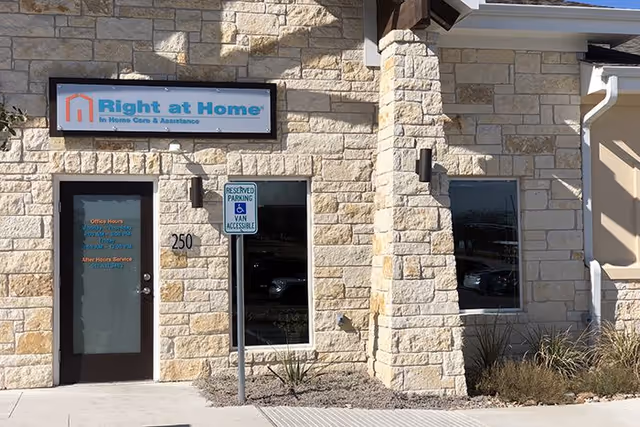 Stone-faced building exterior with Right at Home sign, entrance door, and parking sign.