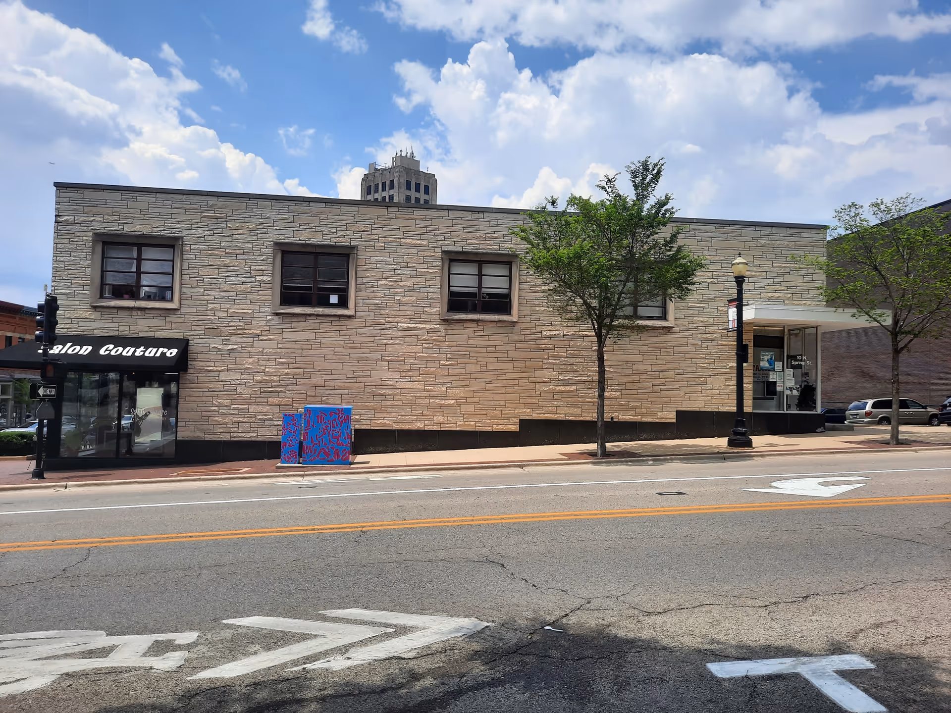 Street-level view of a brick building with storefronts and trees along the sidewalk.