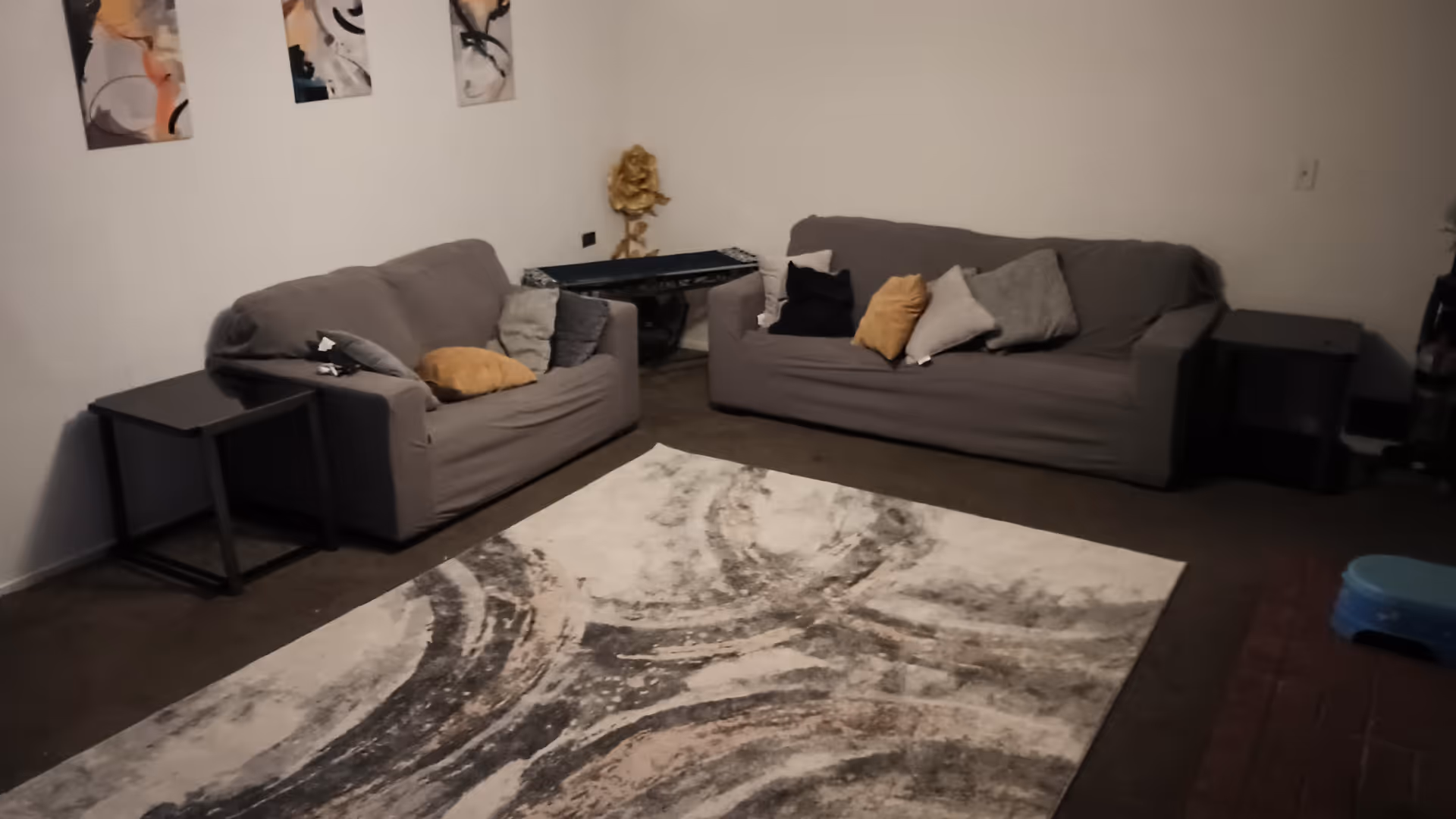 Two gray sofas arranged around a large abstract-patterned rug in a dim living room.