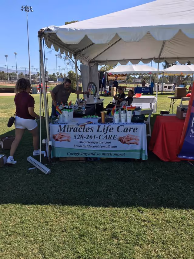 Outdoor tent booth for Miracles Life Care at an event with tables and volunteers.