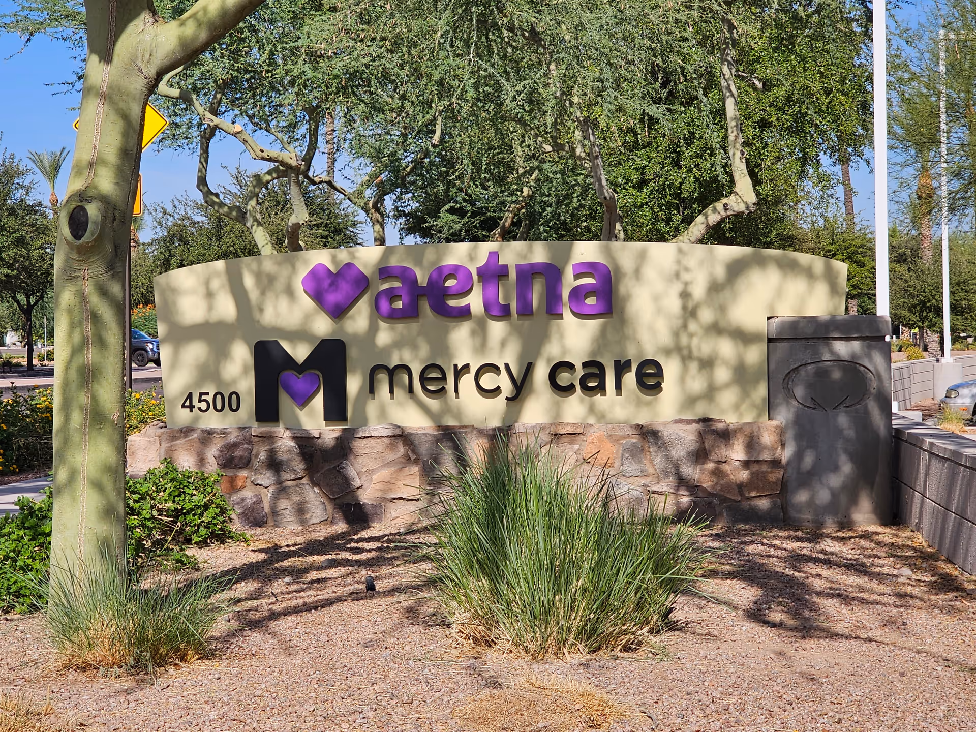 Outdoor entrance sign for Aetna Mercy Care with landscaping and trees.