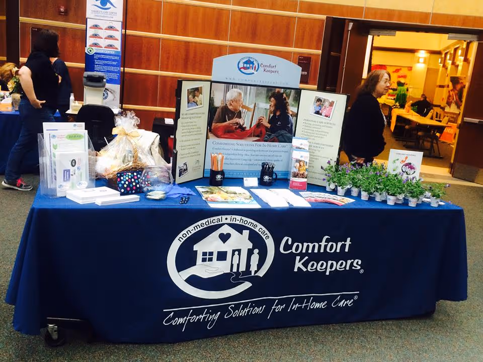 Promotional Comfort Keepers Home Care display table in a lobby with brochures and plants.
