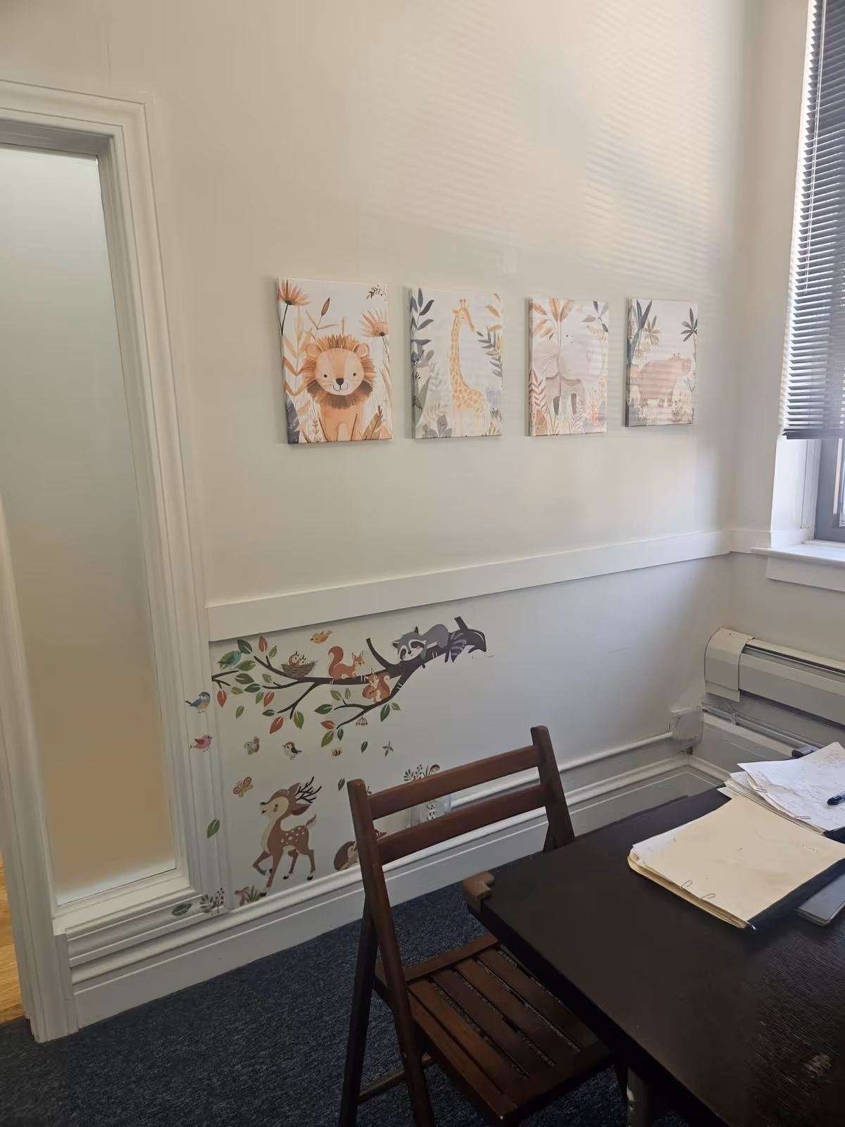 Office-like interior with desk, chair, papers, and animal-themed wall art.