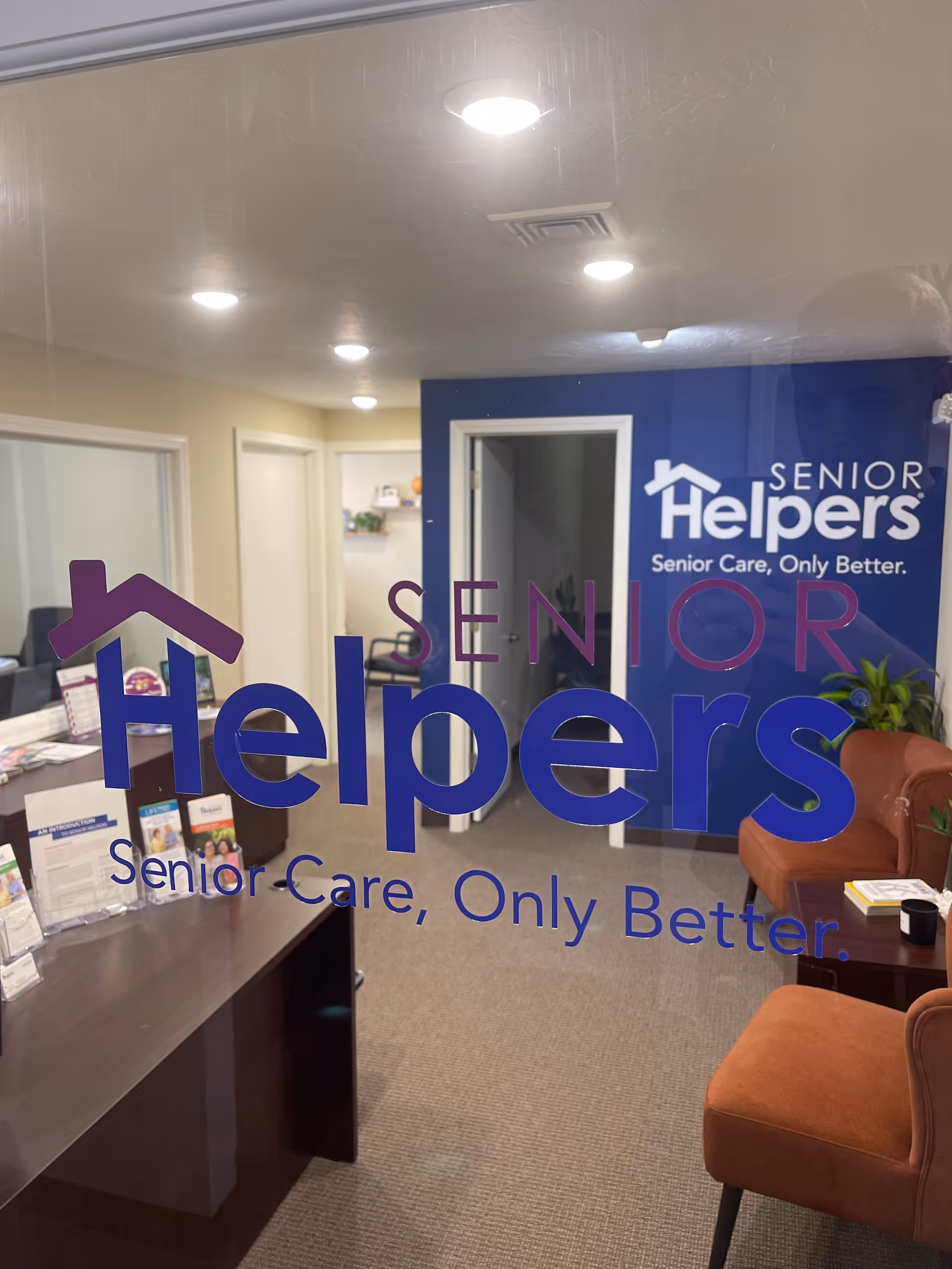 Interior reception area with blue Senior Helpers logo on glass and seating.
