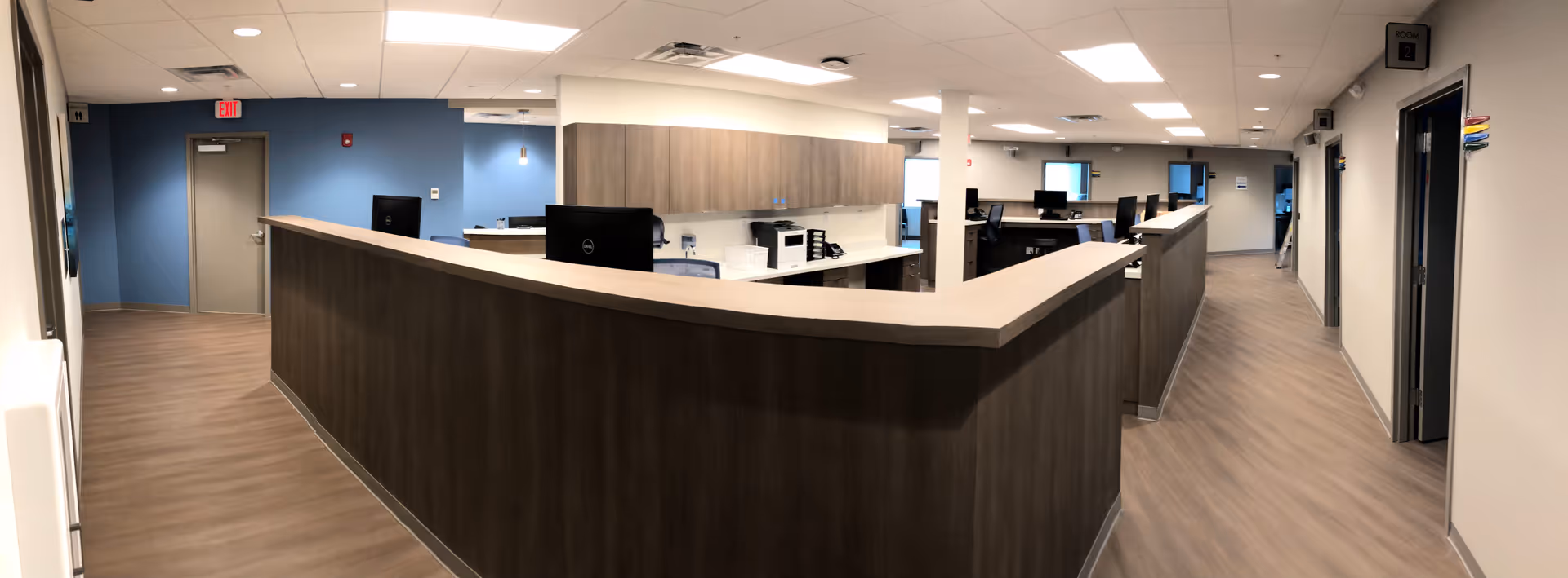 A curved wooden reception desk in a modern clinical lobby with computer workstations.