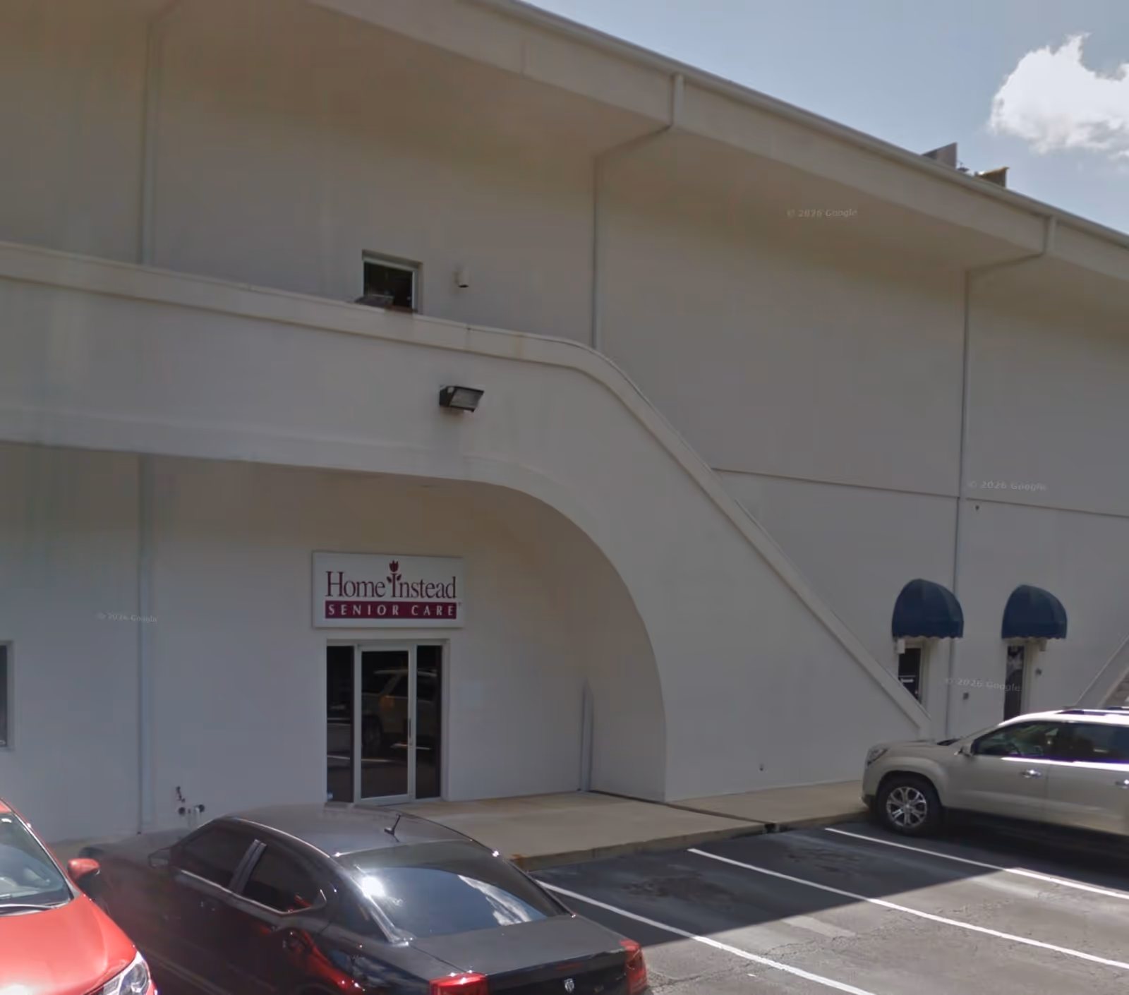 Exterior of a Home Instead Senior Care building with a curved entrance and parked cars.