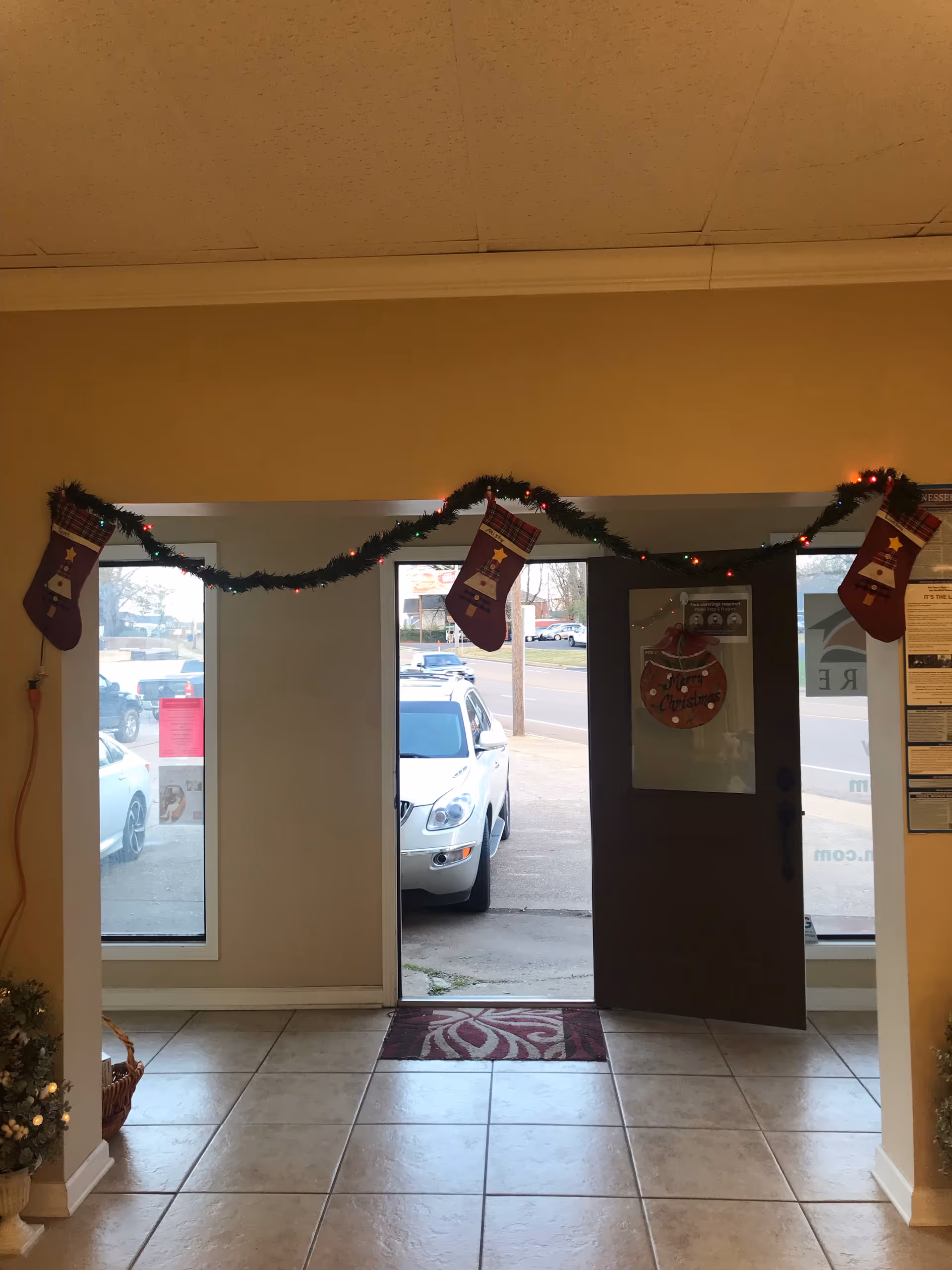 Interior lobby with holiday garland and stockings, open door to outside car view.