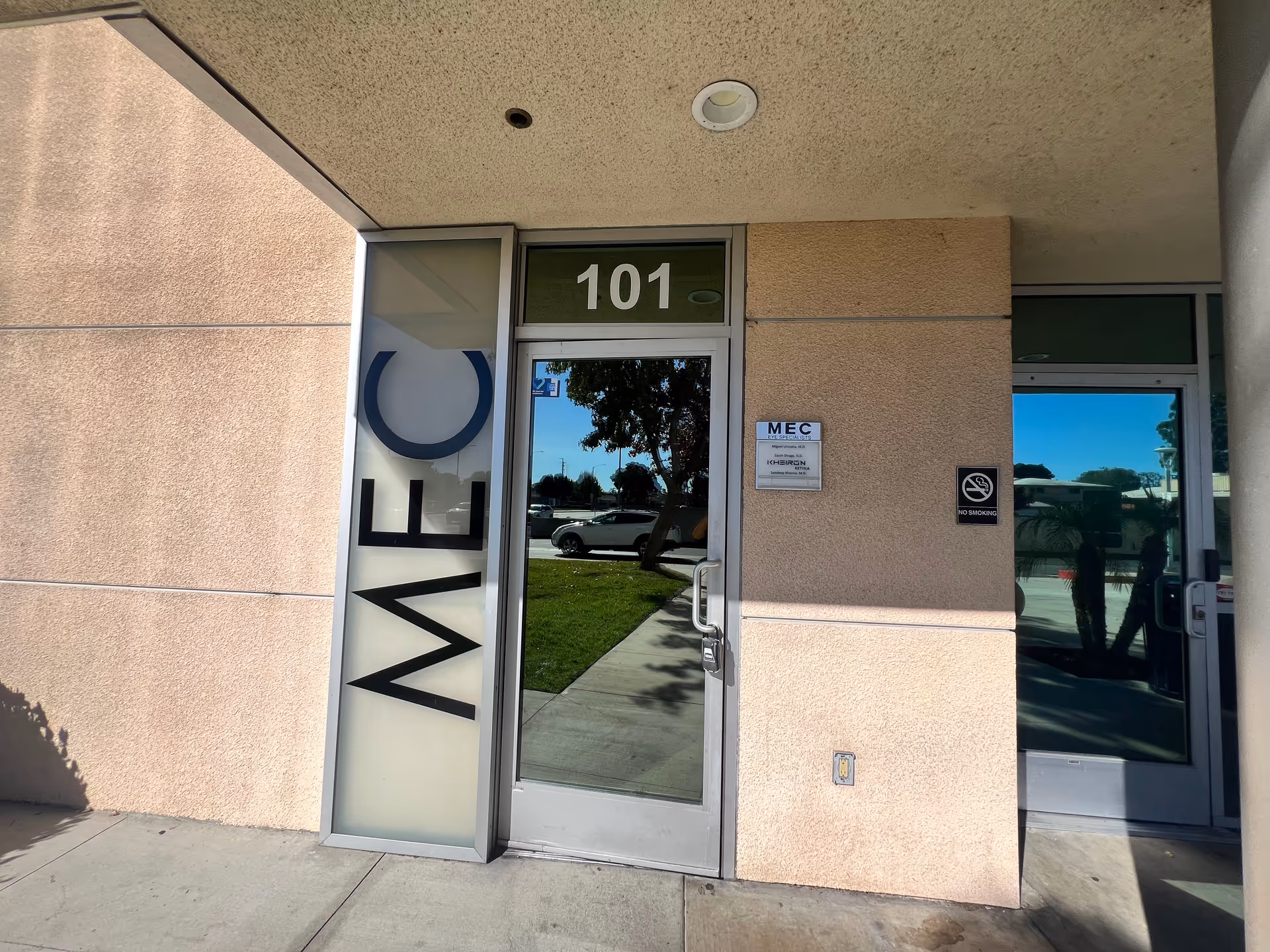 Exterior building entrance with glass door marked 101 and no-smoking sign.