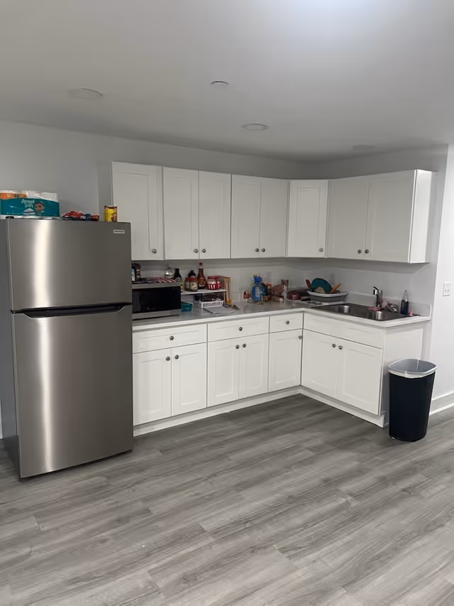 Modern white kitchen with stainless refrigerator, microwave, and sink along counter space.