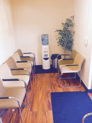 A small waiting area with beige chairs, a water cooler, plant, and blue floor mat.