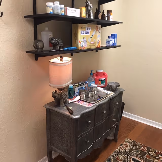 A small vanity area with a dresser, lamp, and shelves stocked with medical supplies.