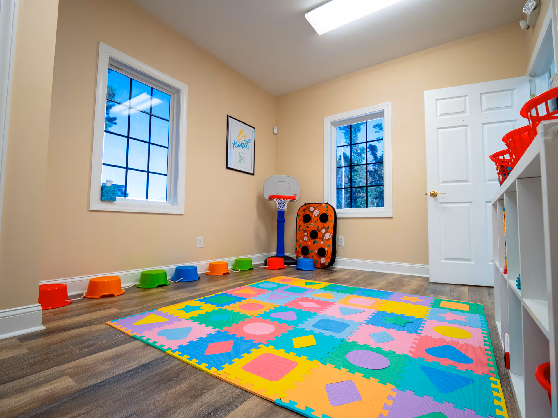 This is a colorful children's playroom with a foam mat, stools, hoops, and shelves against walls.