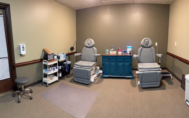 Two gray reclining treatment chairs with a central cabinet and supplies.