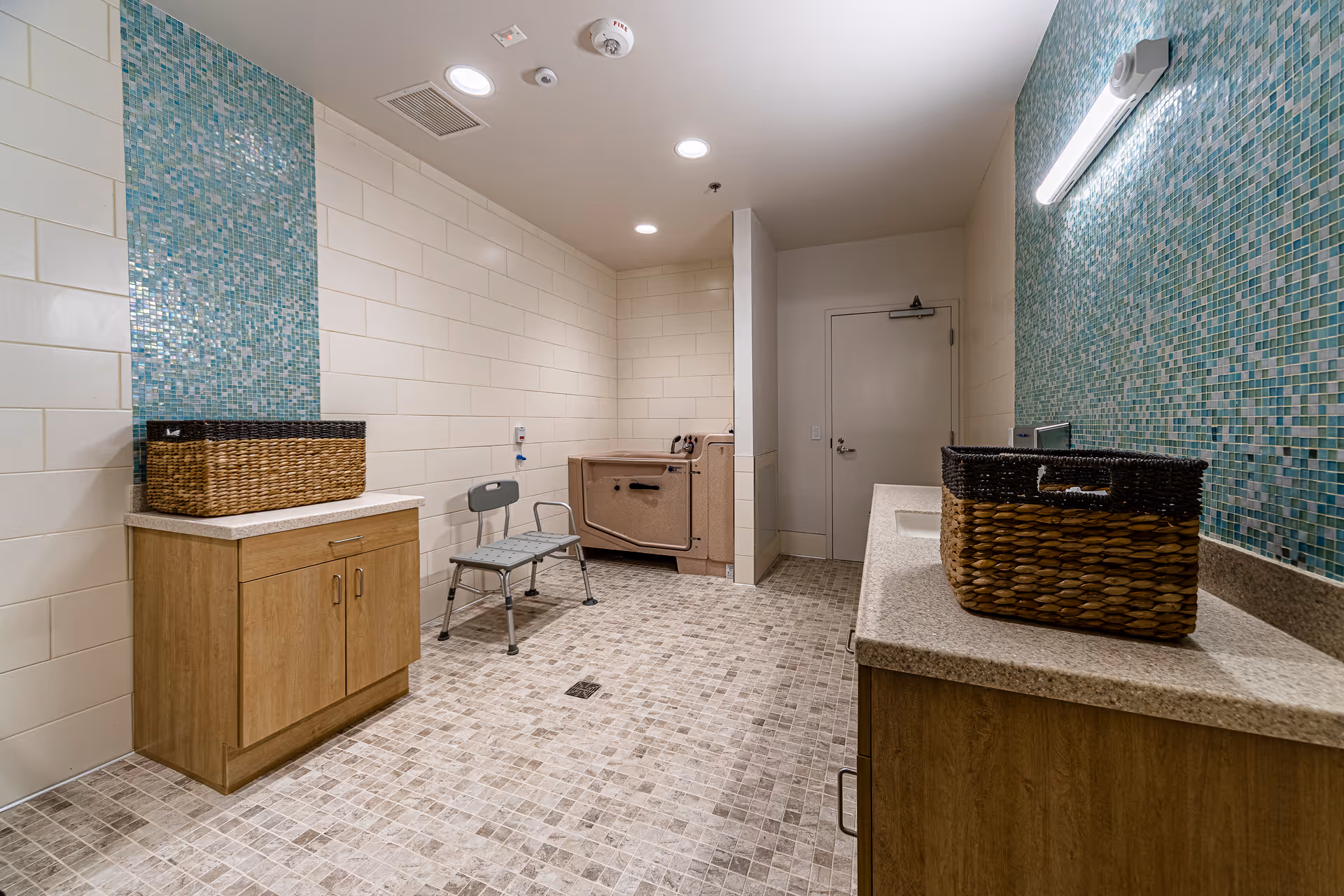 A tiled senior living bathroom with sinks, cabinets, baskets, and teal mosaic walls.