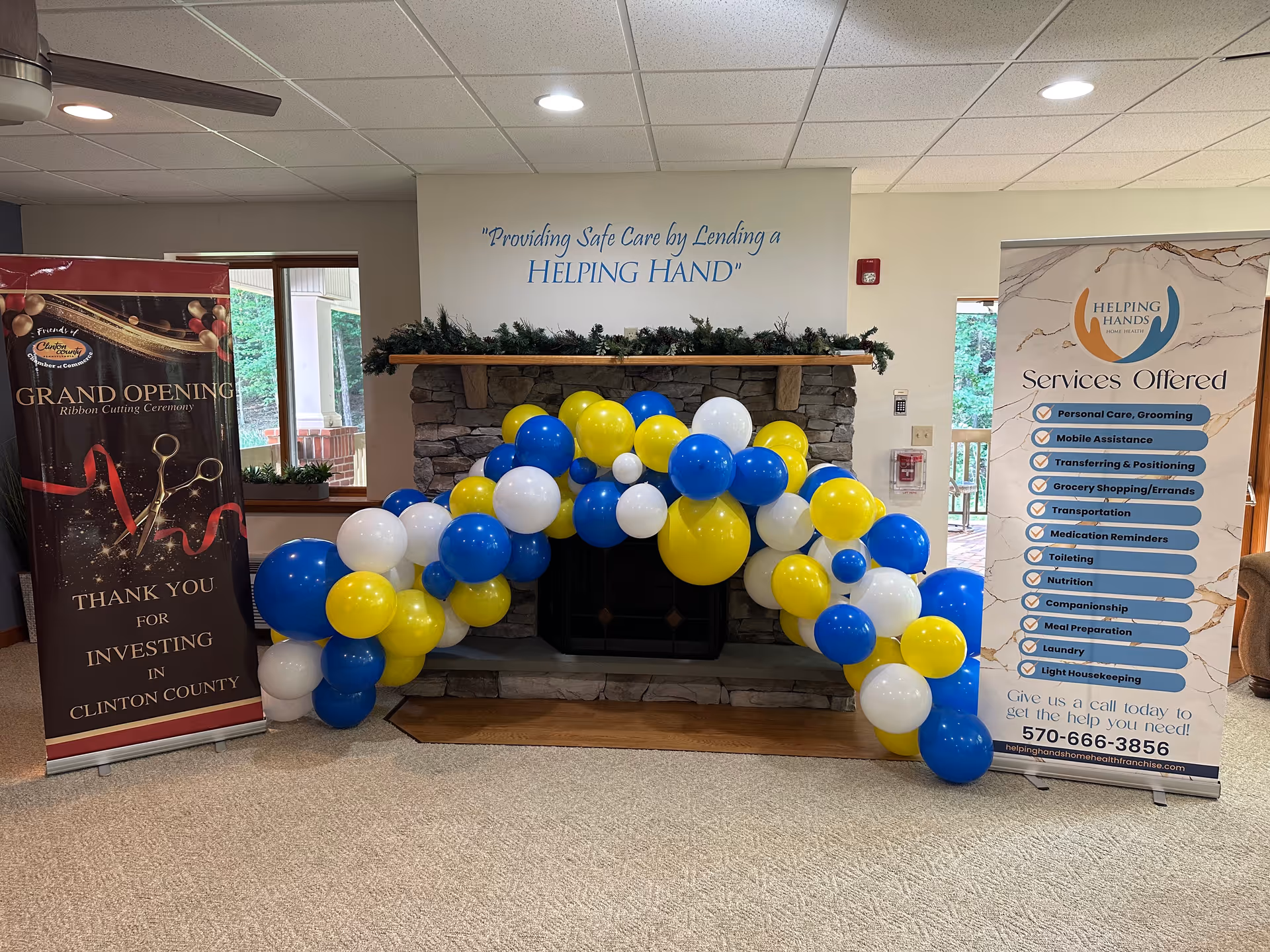 Indoor lobby with a stone fireplace and a blue, yellow, and white balloon arch.