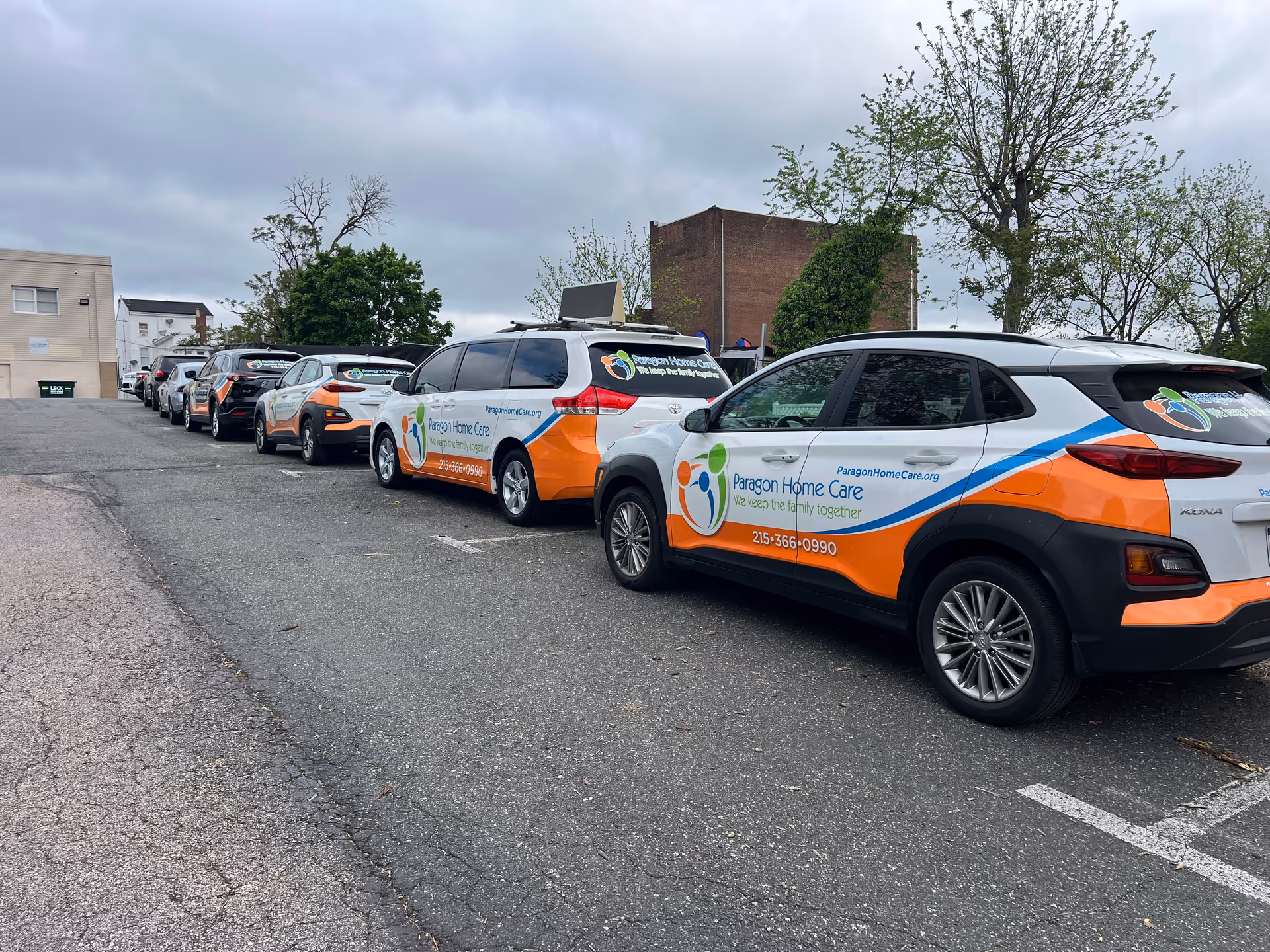 Line of Paragon Home Care vans parked in a lot beside a building.