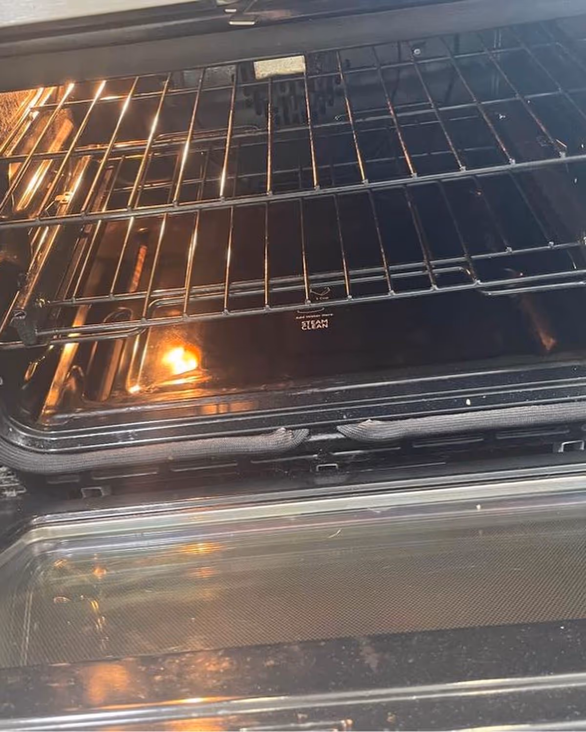 Open oven with metal racks and interior light, showing steam-clean label.