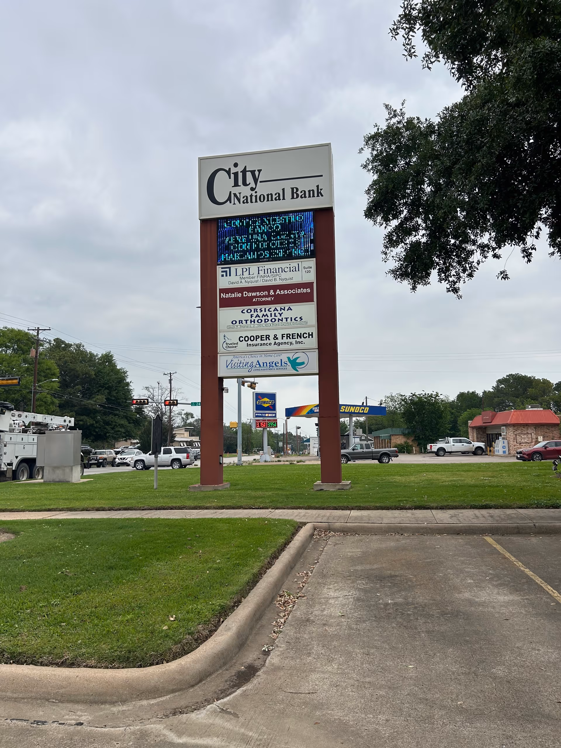 Tall outdoor signboard for City National Bank with nearby businesses in a parking lot.