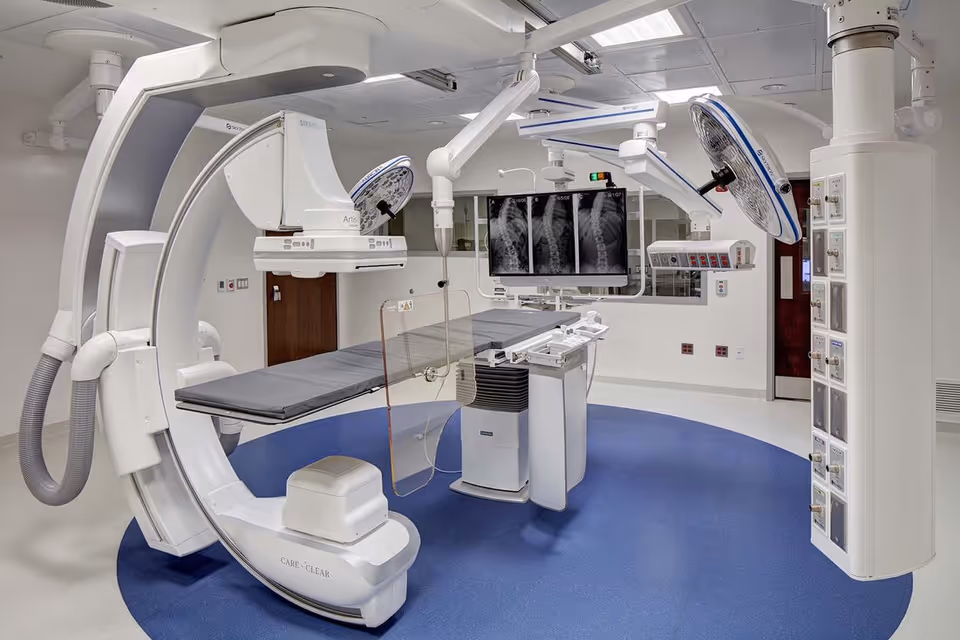 A high-tech surgical suite with C-arm imaging, patient table, monitors, and overhead lighting.