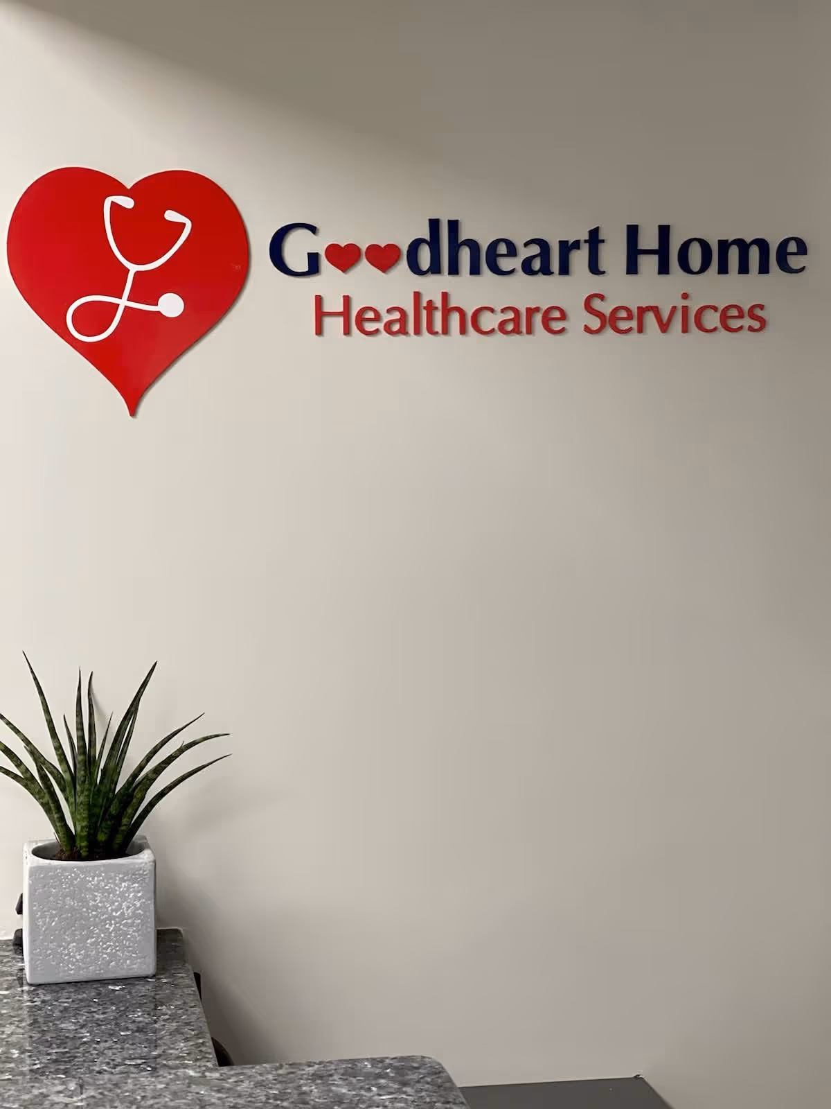 Interior wall with Goodheart Home Healthcare Services sign and a potted plant on a granite counter.