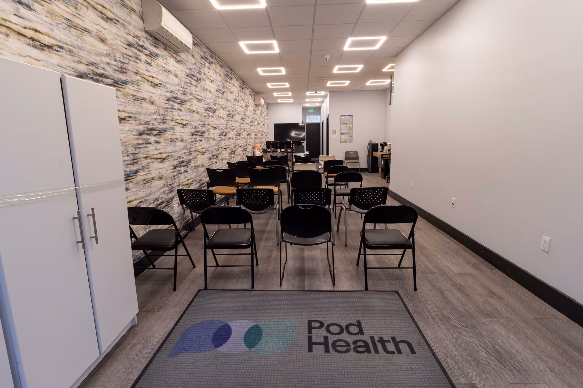 Interior hallway and meeting space with rows of black chairs and a Pod Health logo mat.