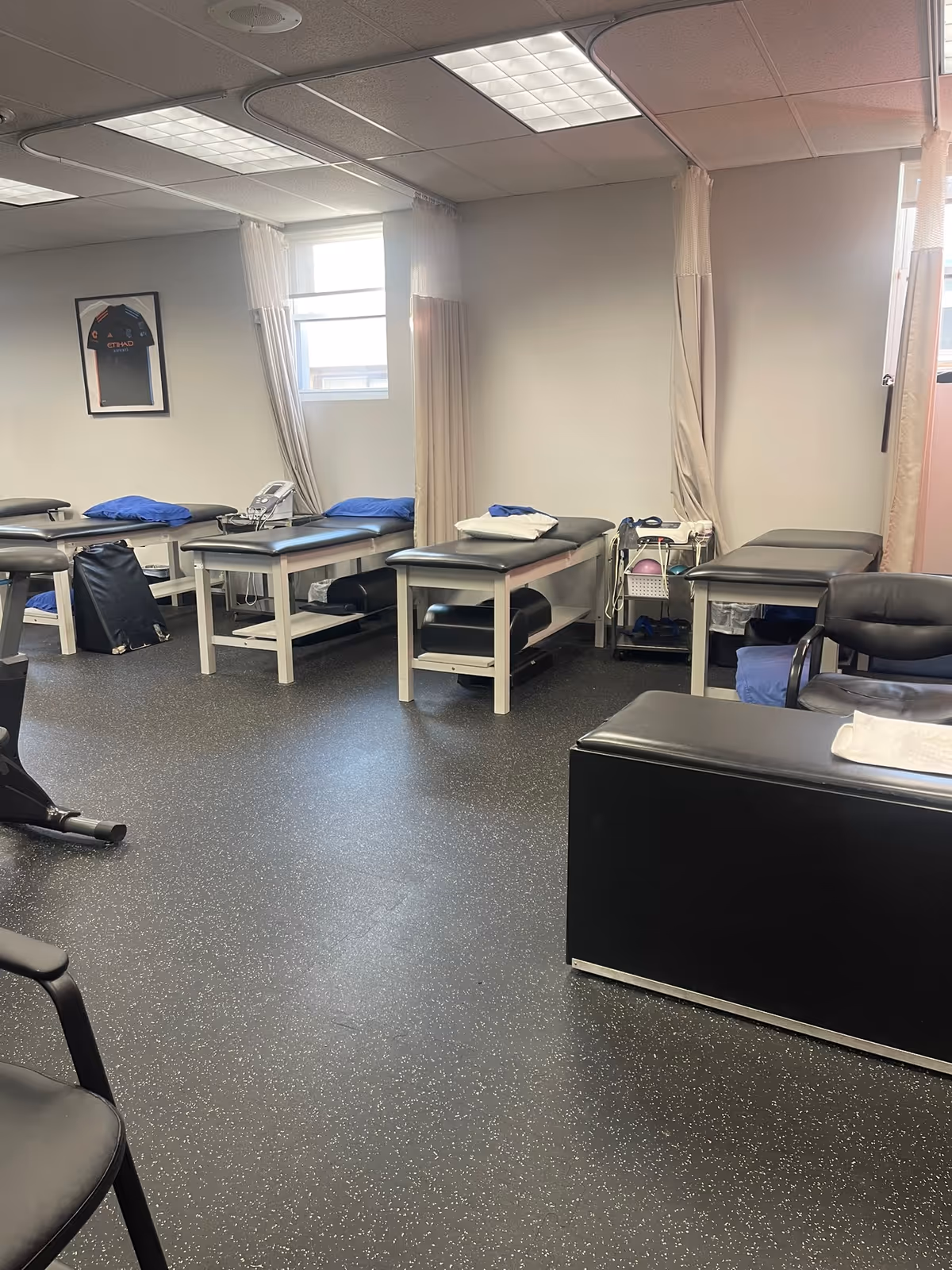 A physical therapy treatment room with several treatment tables, curtains, and medical equipment.