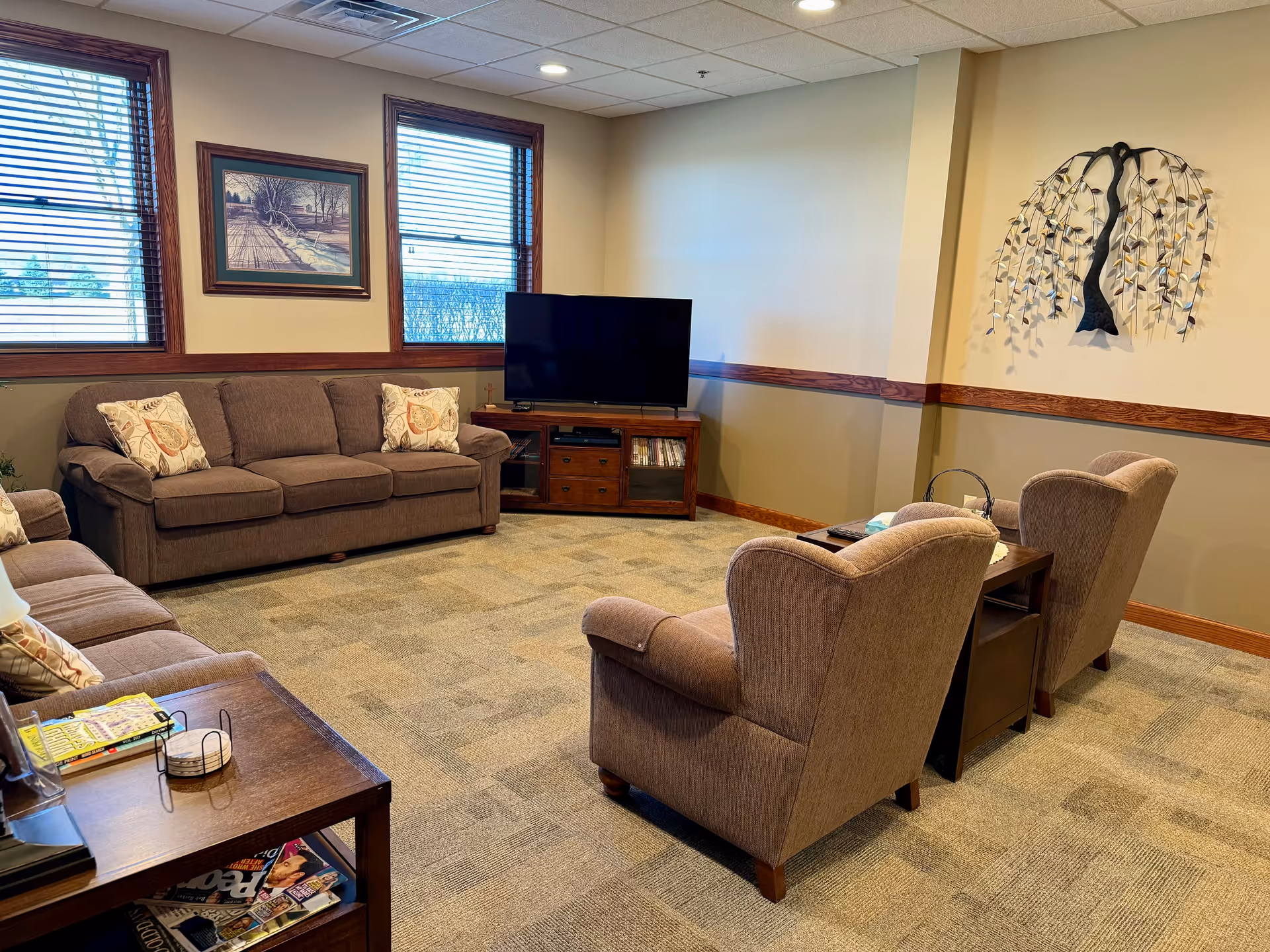 Cozy senior living lounge with couches, armchairs, a coffee table, and a TV.