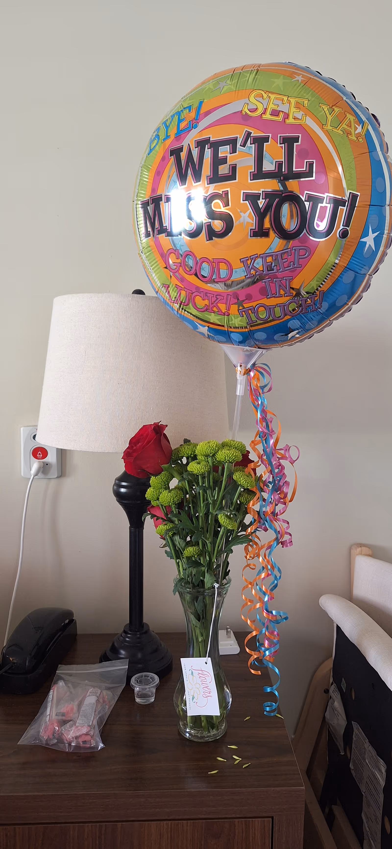 Indoor resident room featuring a lamp, flowers, and a large 'We'll Miss You' balloon.