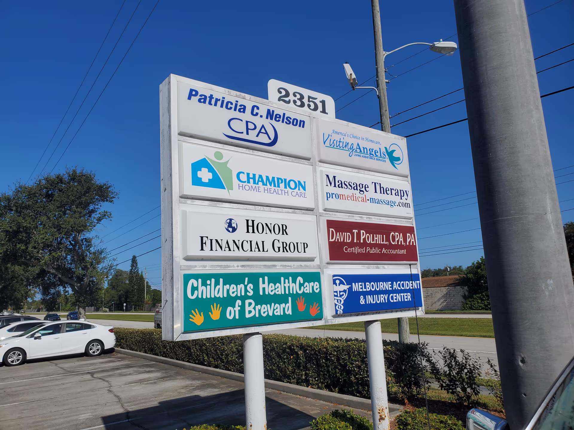 Outdoor signboard with multiple business ads including Visiting Angels near a parking lot.