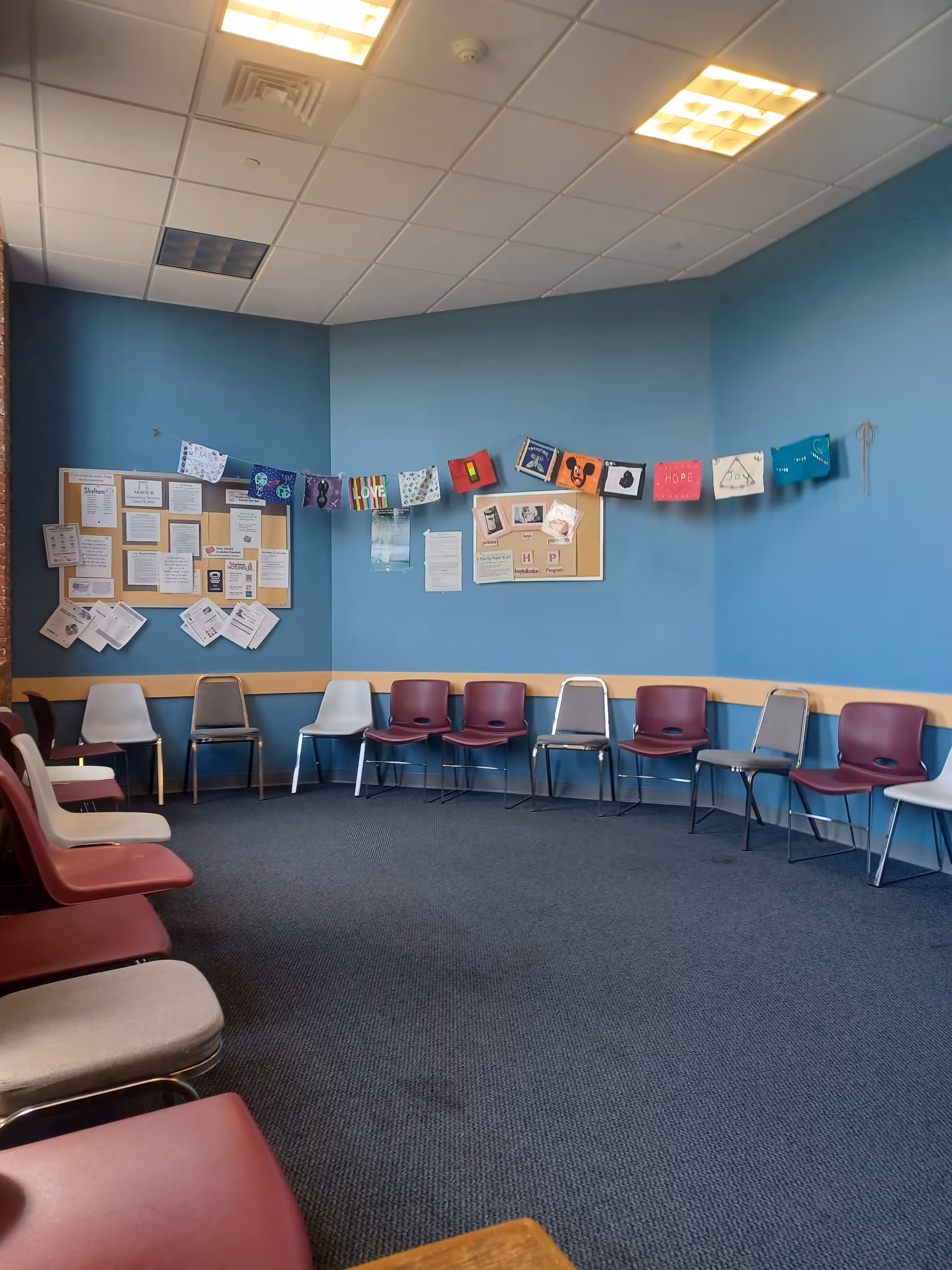 Blue-walled activity room with numerous chairs arranged around the perimeter and bulletin boards.