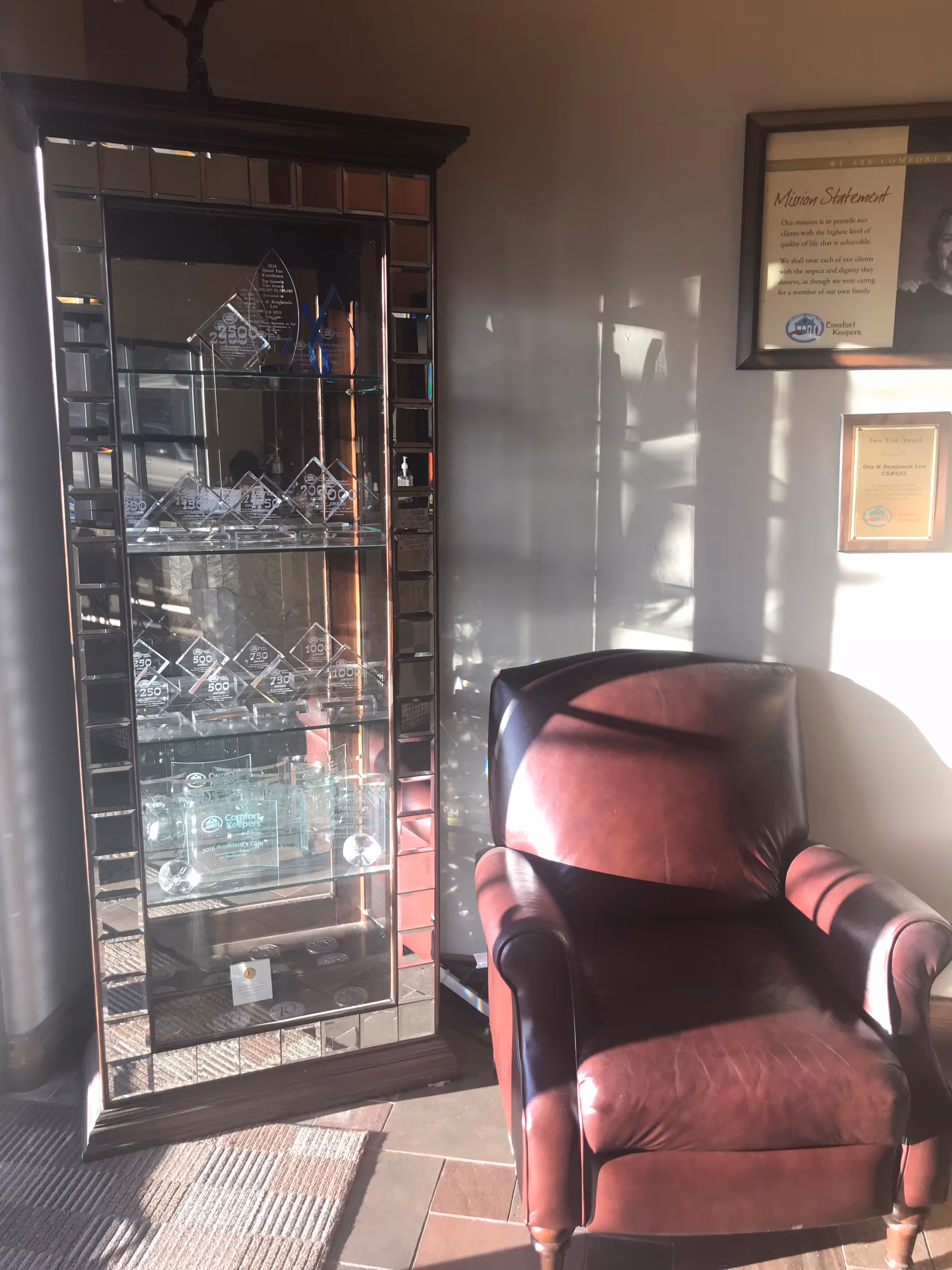 Glass display cabinet with crystal awards beside a burgundy leather chair in a lobby corner.