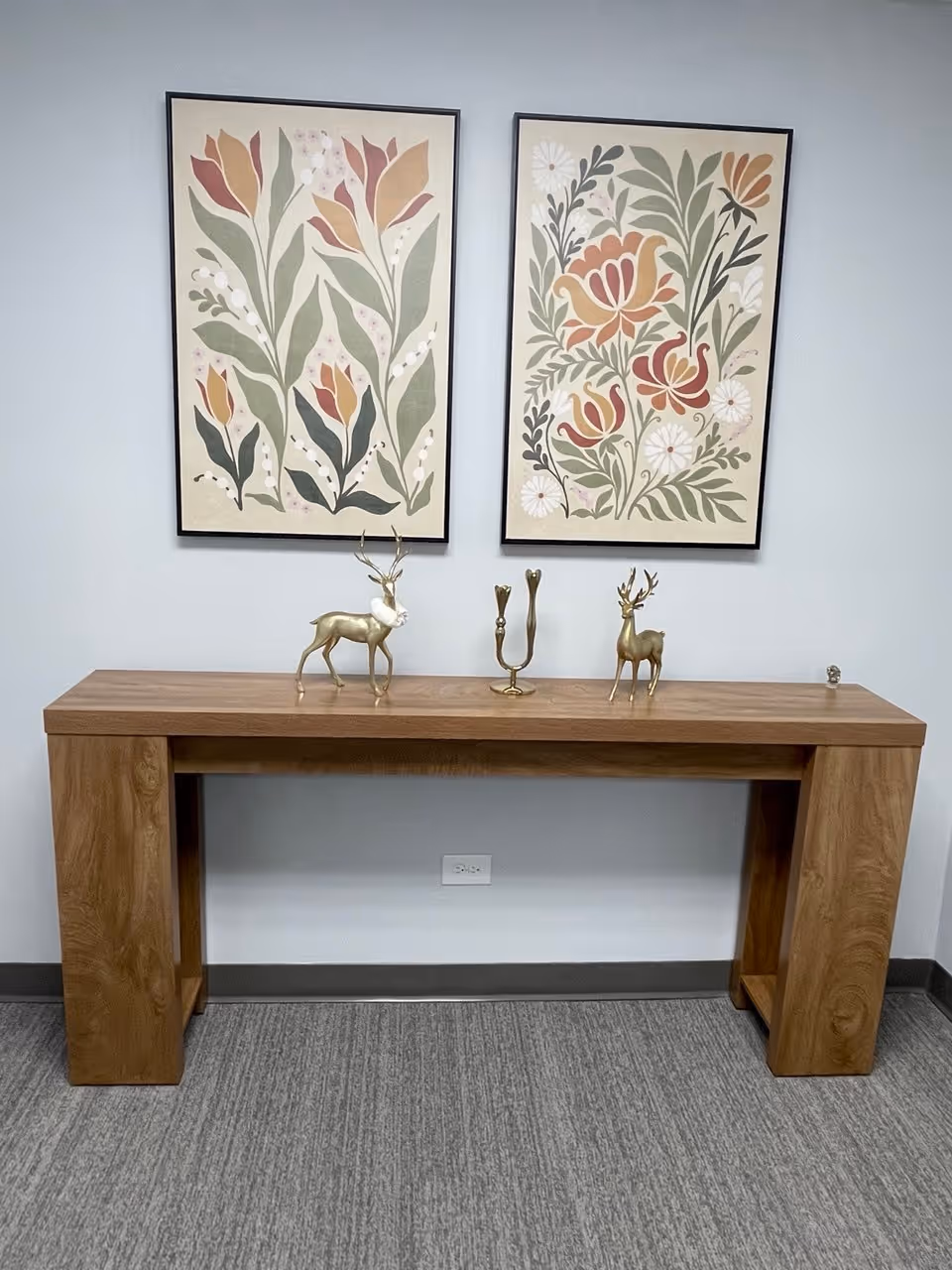 A wooden console table with botanical prints and decorative brass deer figurines against a blue wall.
