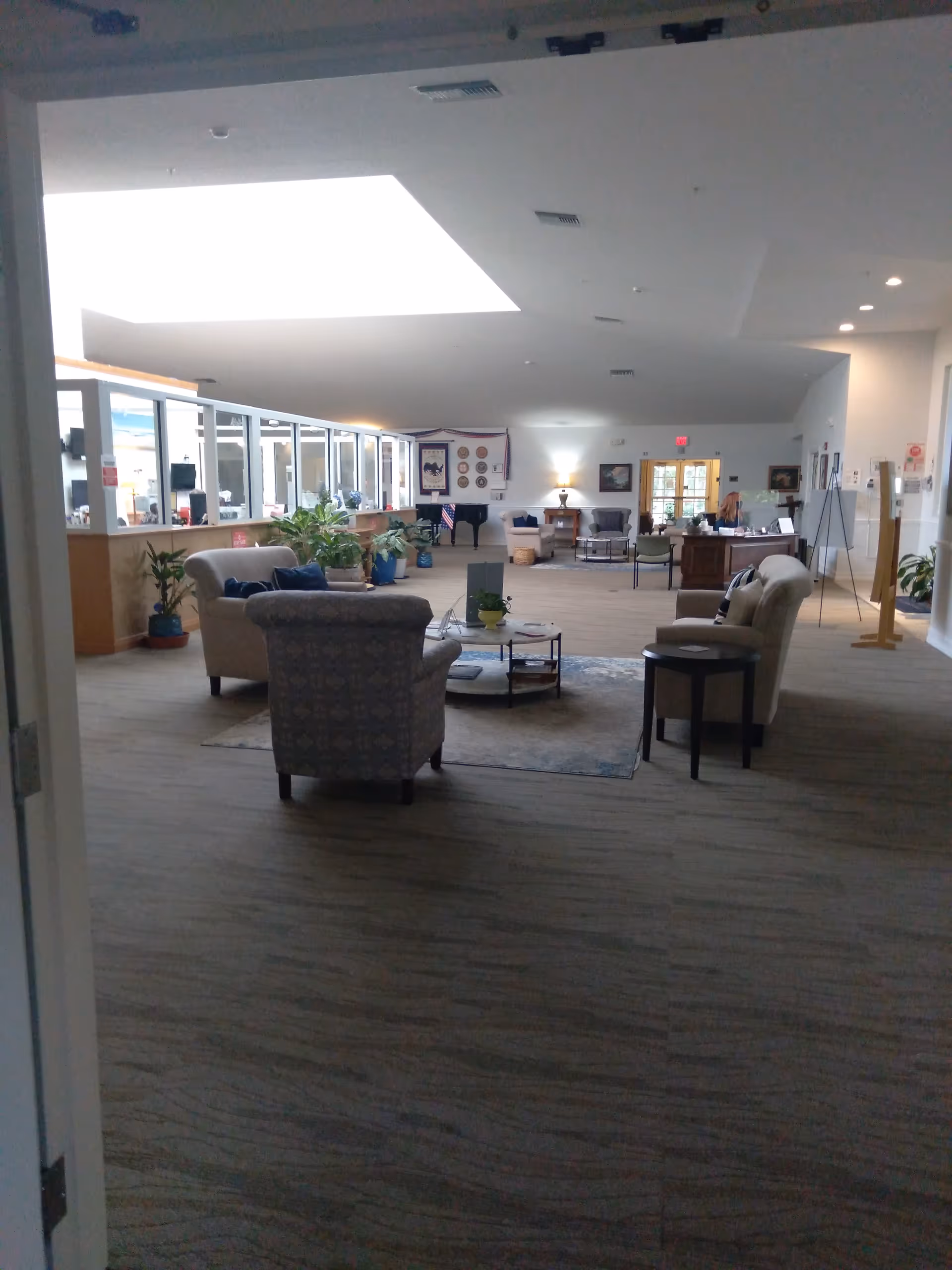Spacious hospice lobby with sofas, tables, plants, and a reception area.