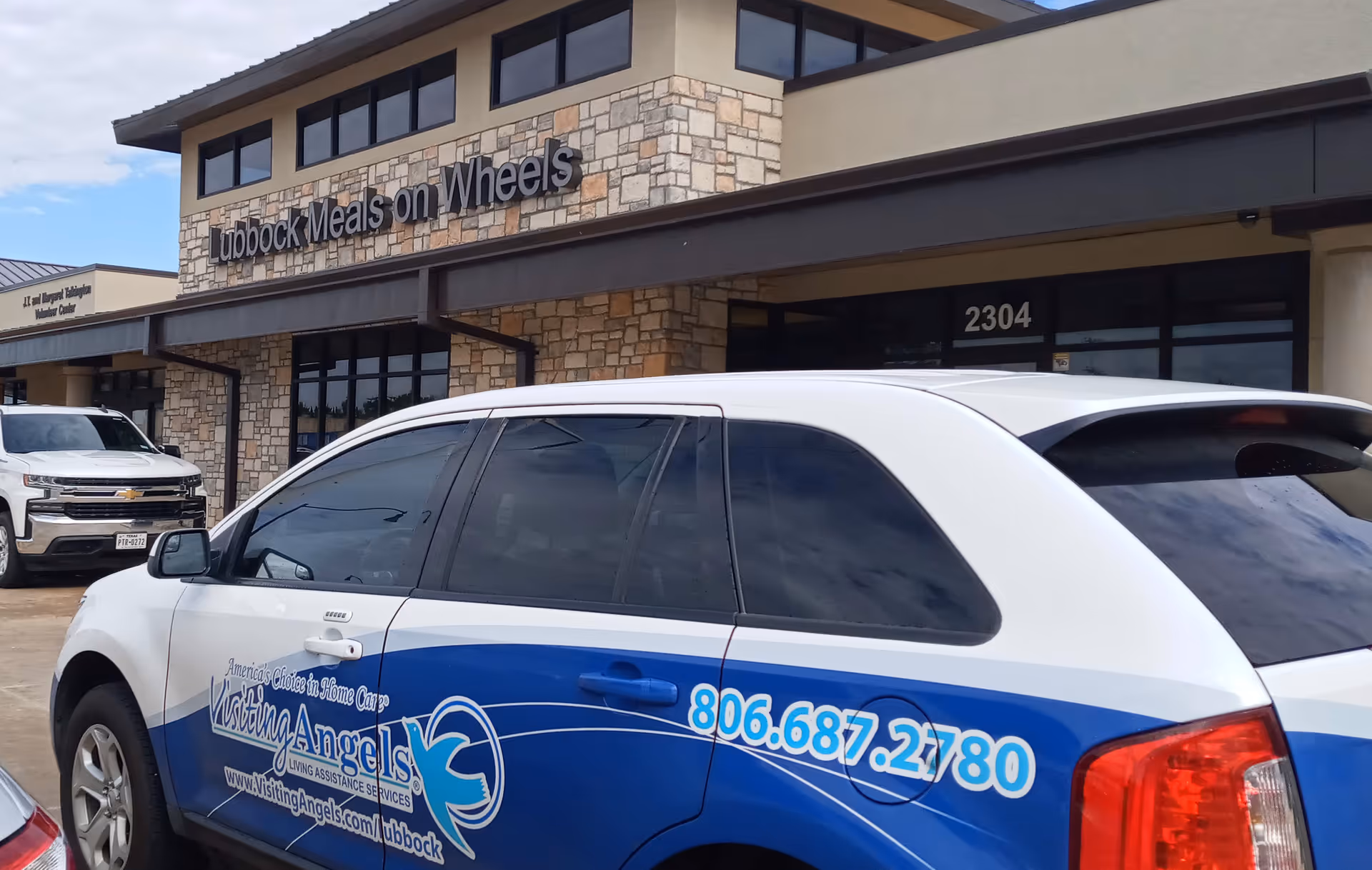 Exterior view of a stone-front building with Lubbock Meals on Wheels sign and Visiting Angels vehicle.