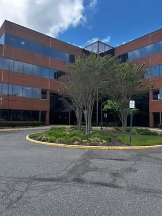 Brick multi-story building with blue-tinted windows and a landscaped circular driveway.