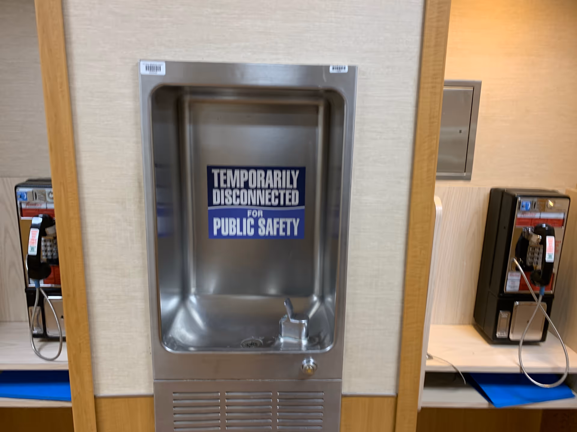Stainless steel drinking fountain in a hallway with a temporary disconnection sign.