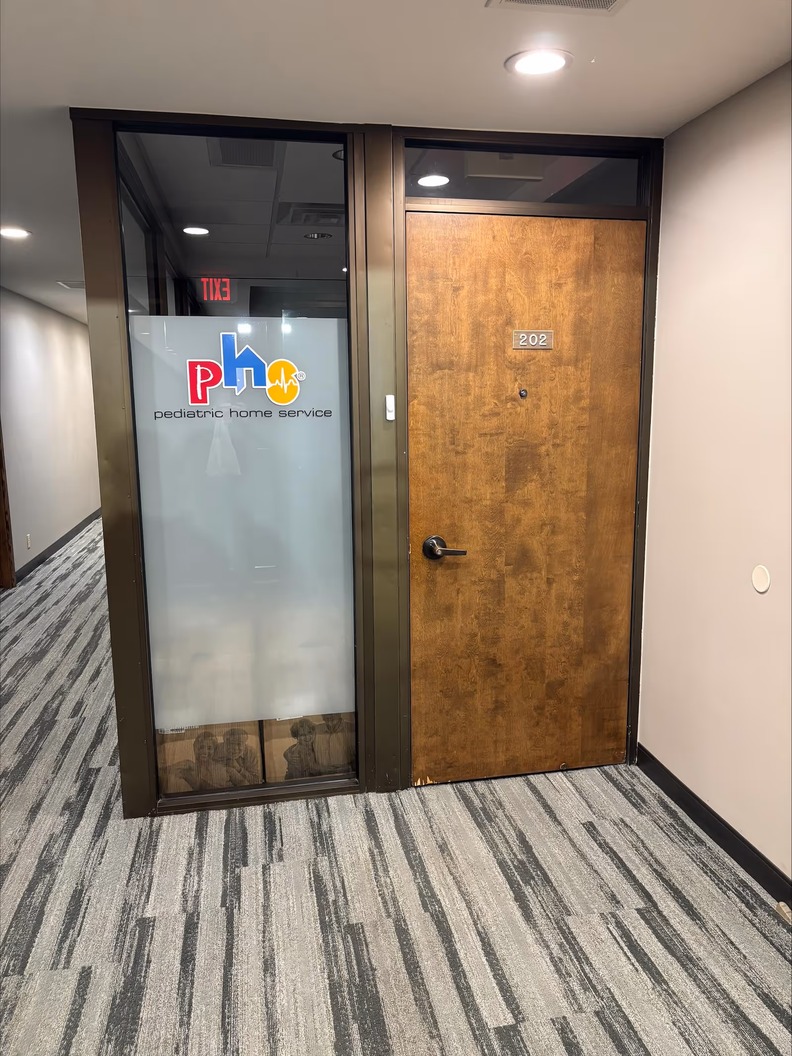 Hallway with glass partition showing Pediatric Home Service logo beside a wooden door labeled 202.