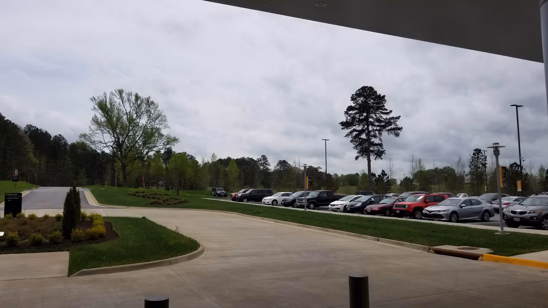 A curved driveway leads to a parking lot with many cars and trees.