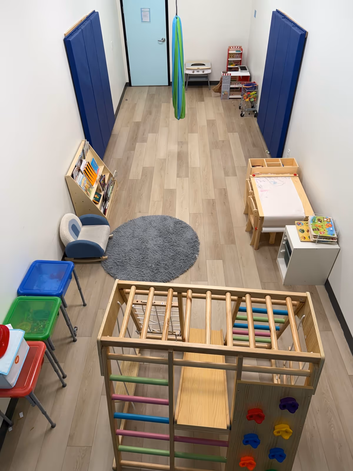 Therapy playroom with padded walls, climbing frame, toys, and activity stations.