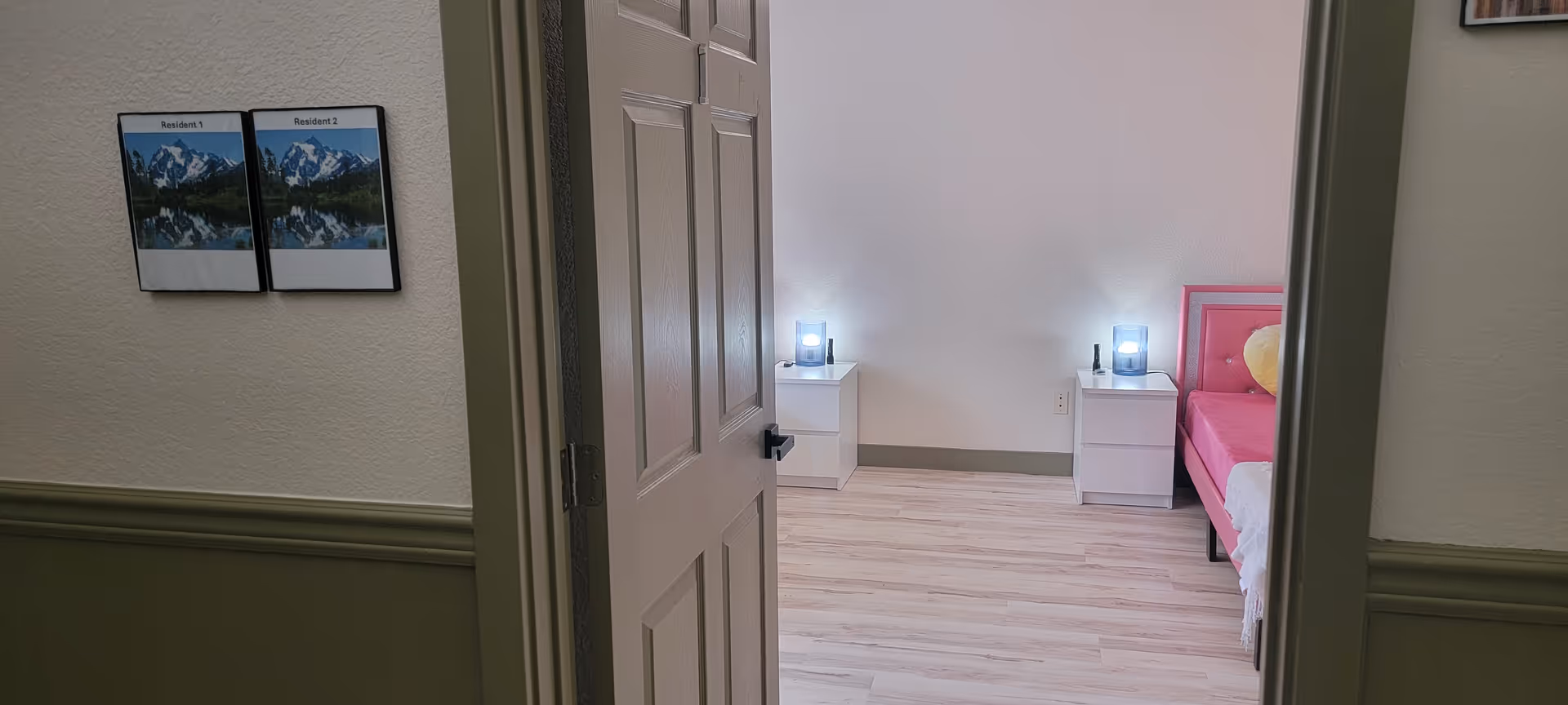 Open doorway reveals a bright bedroom with two nightstands, lamps, and a pink bed.