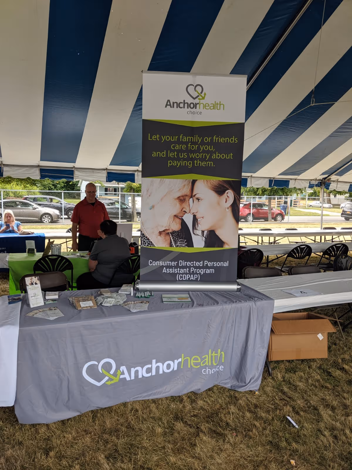 Outdoor striped blue and white tent with Anchor Health Choice banner and promotional tables.