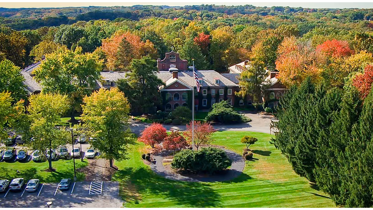 Aerial view of a large senior living campus with trees, parking, and a flagpole.