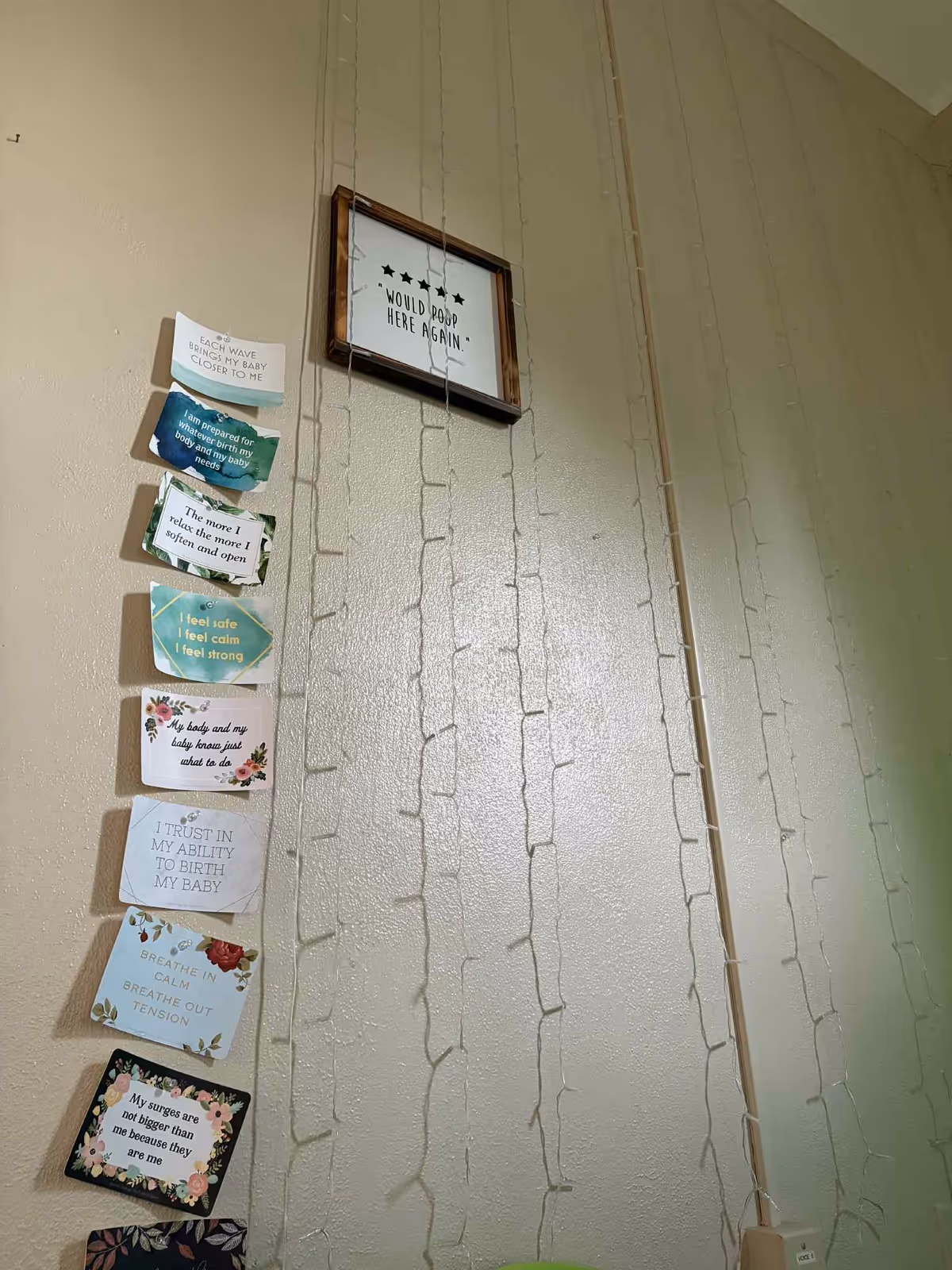 Tall beige wall with hanging inspirational cards and string lights in a hallway.