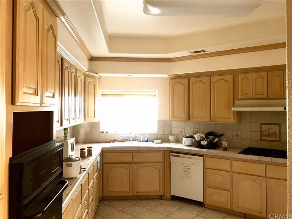 Bright L-shaped kitchen in a senior living facility with wooden cabinets and appliances.