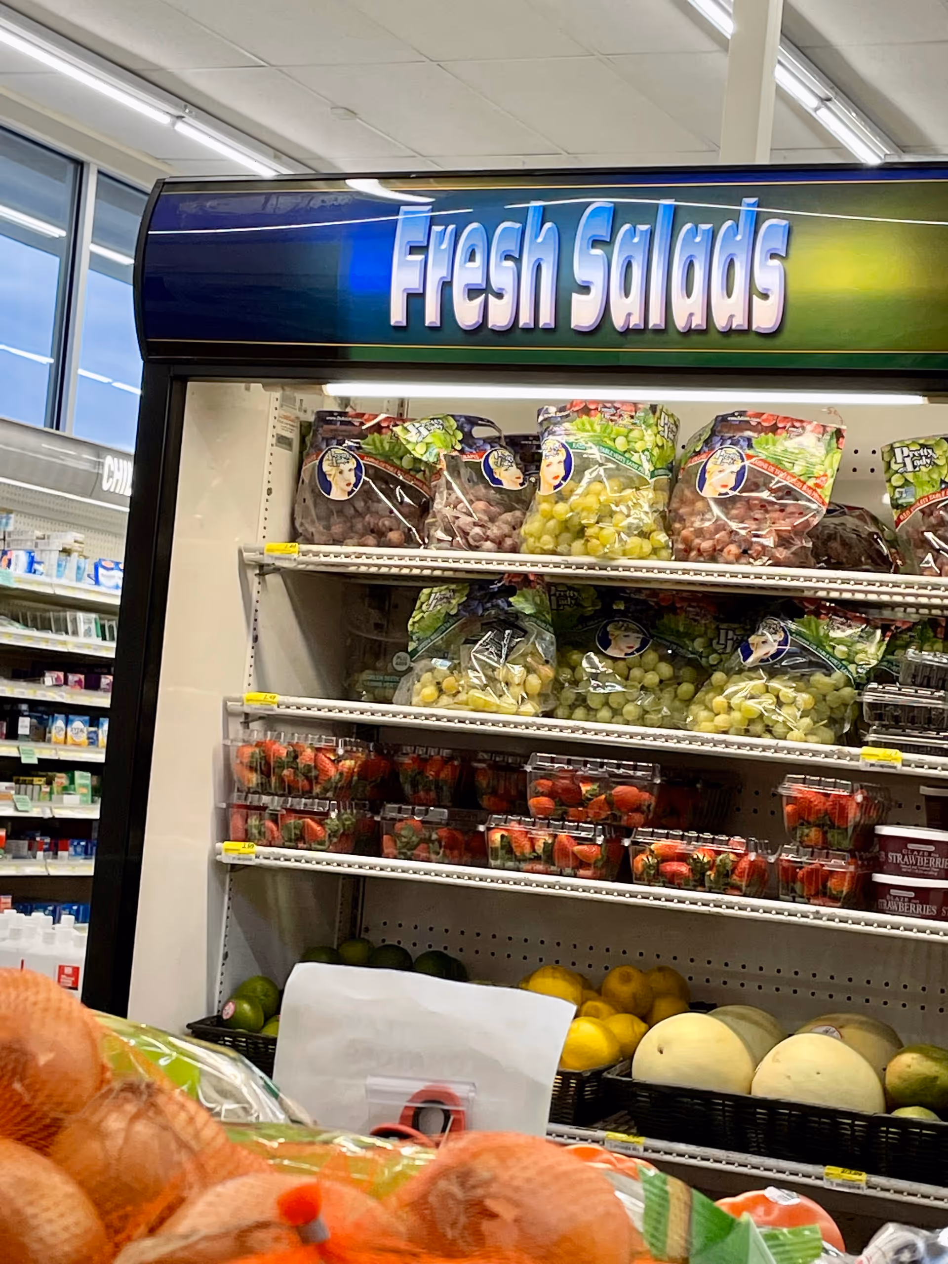 Produce section with bagged salads and assorted fruits near 'Fresh Salads' sign.
