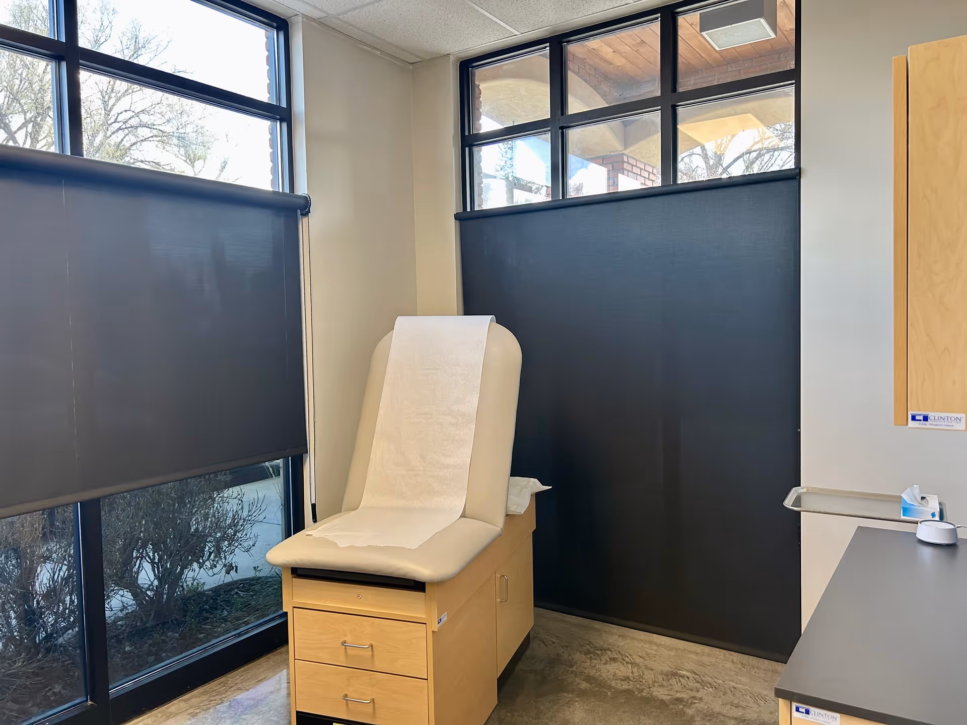 Medical exam chair with paper sheet in a clinic room with dark blinds.