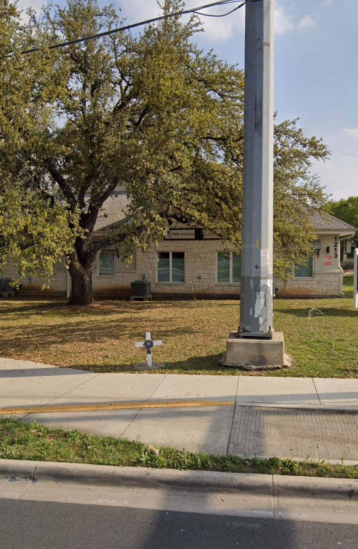A single-story senior living building visible from the sidewalk with a large tree.