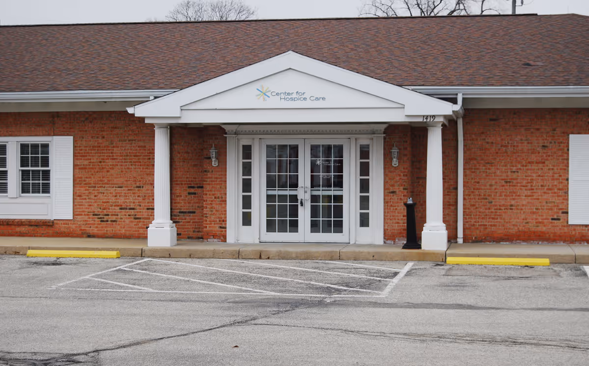 Brick facility entrance with white columns, glass doors, and a Center for Hospice Care sign.